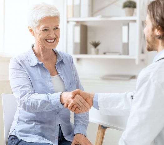 Happy senior woman handshaking with personal doctor at office